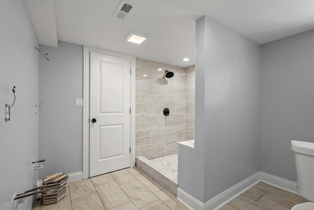 full bathroom featuring toilet, visible vents, a tile shower, and baseboards