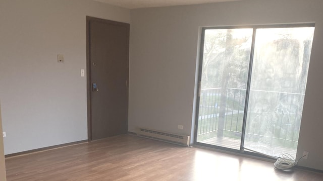 empty room with hardwood / wood-style floors, a wealth of natural light, and baseboard heating