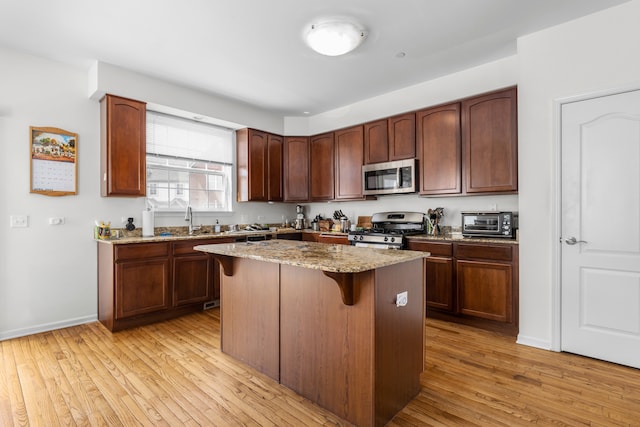 kitchen featuring a center island, a breakfast bar, light hardwood / wood-style flooring, stainless steel appliances, and light stone counters