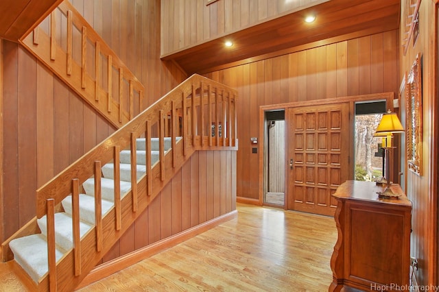 entryway with high vaulted ceiling, light hardwood / wood-style flooring, and wood walls