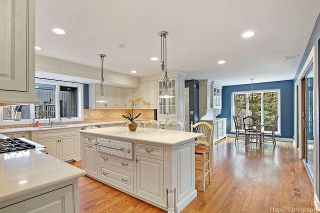 kitchen featuring backsplash, light hardwood / wood-style floors, white cabinets, pendant lighting, and a center island