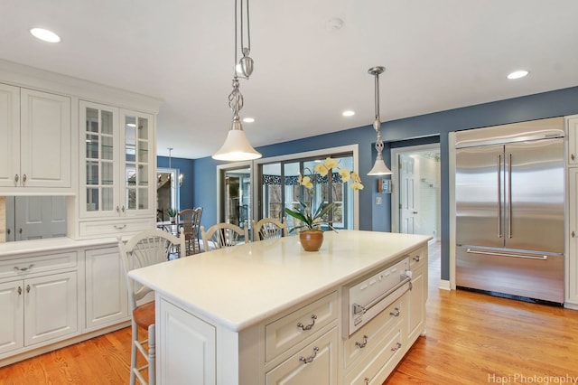 kitchen featuring decorative light fixtures, a kitchen island, built in fridge, and light hardwood / wood-style flooring