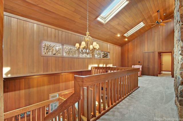 corridor with wooden walls, light carpet, wooden ceiling, a notable chandelier, and a skylight