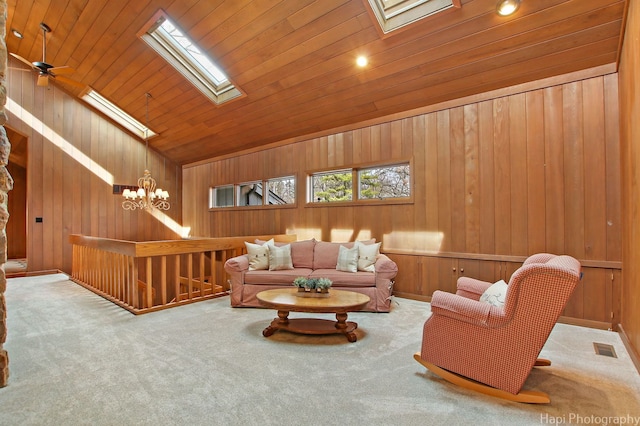 living room with ceiling fan with notable chandelier, wood walls, lofted ceiling with skylight, and light colored carpet