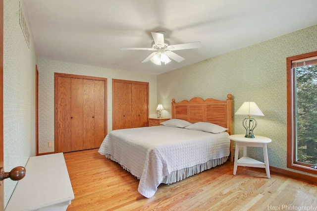 bedroom featuring ceiling fan, two closets, and light hardwood / wood-style floors