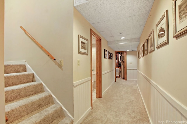 hall with a drop ceiling and light colored carpet