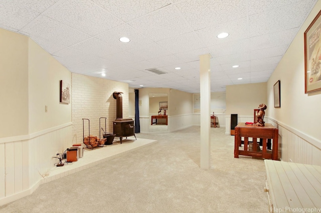 interior space featuring a drop ceiling, a wood stove, light colored carpet, and brick wall