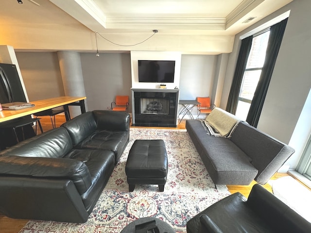 living room featuring hardwood / wood-style floors, crown molding, a tile fireplace, and a raised ceiling