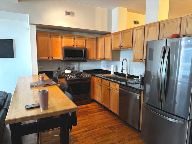 kitchen with dark wood-type flooring, backsplash, sink, black appliances, and a towering ceiling