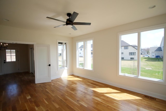 empty room featuring wood finished floors, visible vents, baseboards, and ceiling fan with notable chandelier