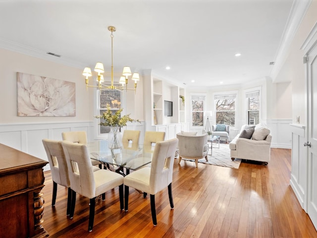 dining room with built in shelves, a decorative wall, visible vents, ornamental molding, and wood-type flooring