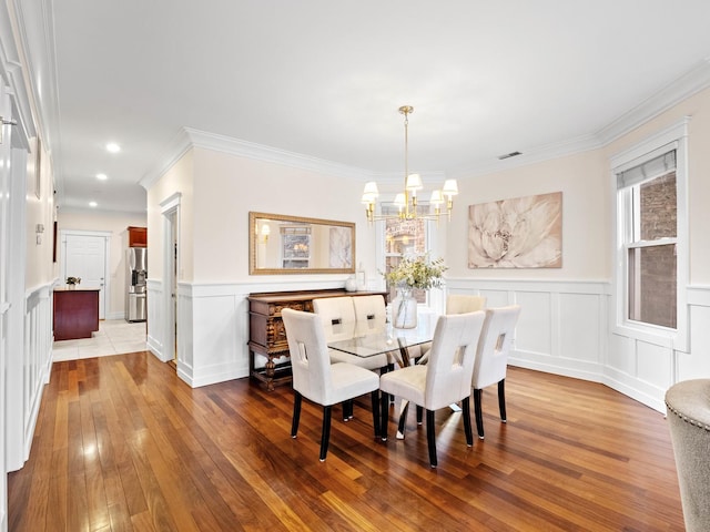 dining room with a chandelier, wood-type flooring, crown molding, and a decorative wall