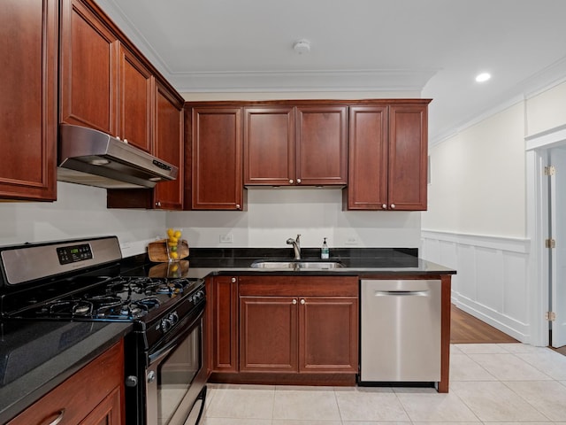 kitchen featuring a wainscoted wall, appliances with stainless steel finishes, ornamental molding, under cabinet range hood, and a sink