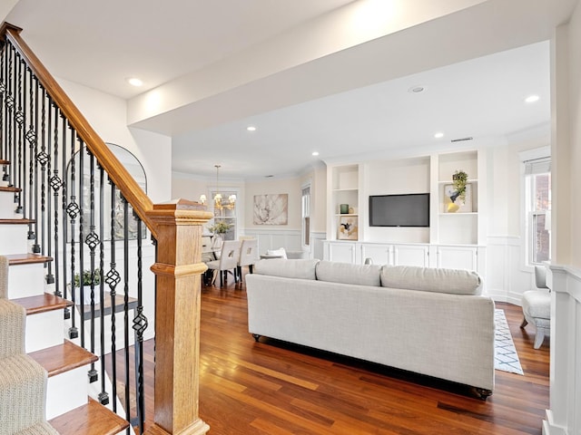 living area with a wainscoted wall, a decorative wall, stairway, wood finished floors, and a chandelier