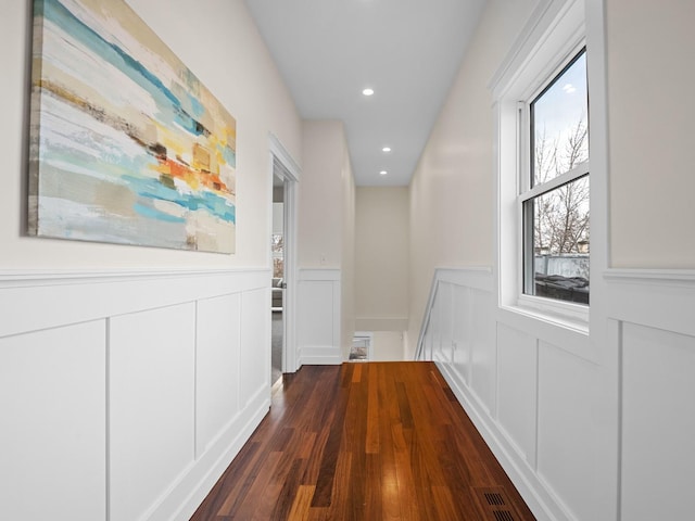 corridor featuring dark wood finished floors, recessed lighting, visible vents, a decorative wall, and wainscoting