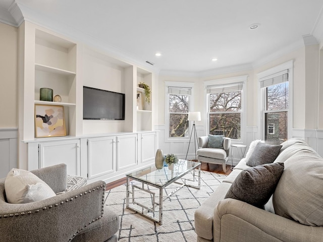 living area featuring built in shelves, ornamental molding, a decorative wall, and light wood finished floors