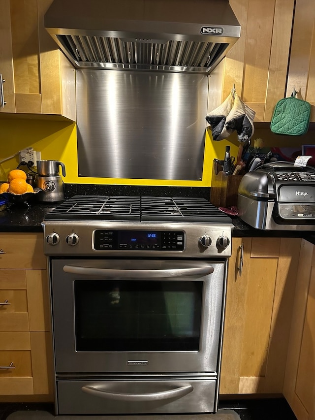 kitchen featuring dark stone counters, wall chimney range hood, and high end stainless steel range