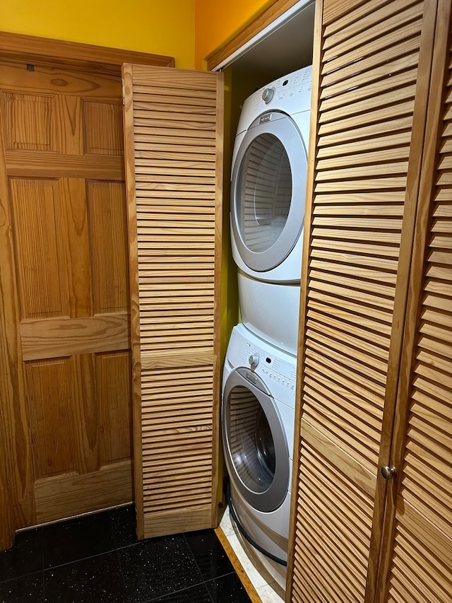 clothes washing area with dark tile flooring and stacked washing maching and dryer