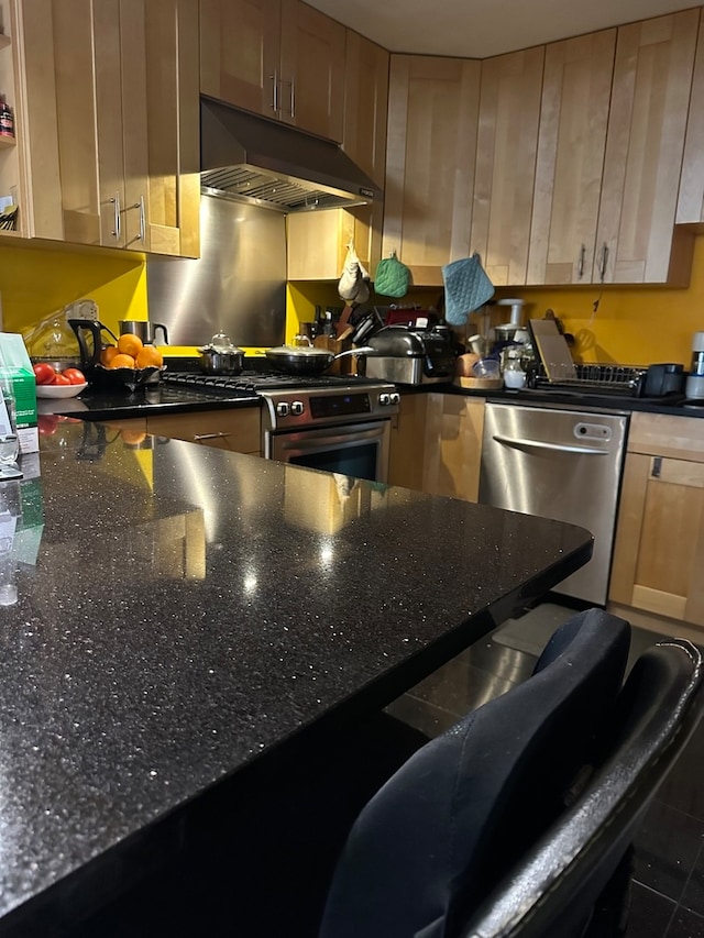 kitchen with appliances with stainless steel finishes, dark stone countertops, and light brown cabinets