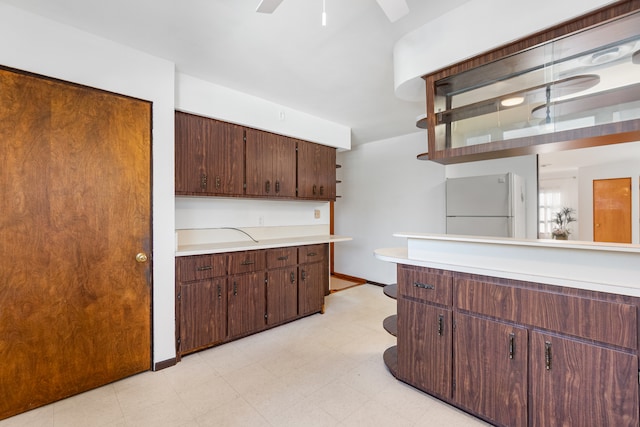 kitchen with dark brown cabinets, light tile flooring, ceiling fan, and white refrigerator