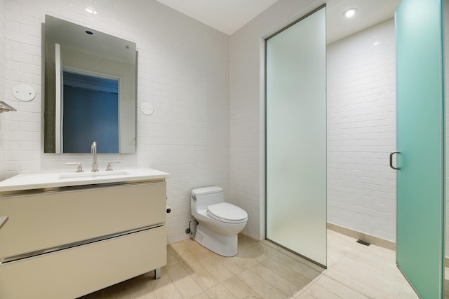 bathroom with vanity, tile walls, toilet, and a shower with door