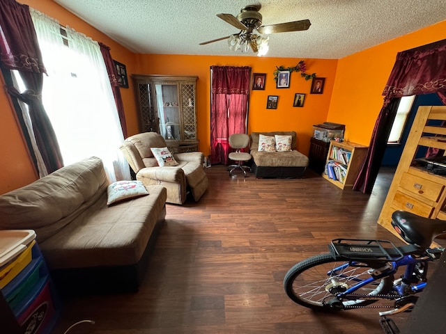 living room featuring dark wood-type flooring, ceiling fan, and a textured ceiling