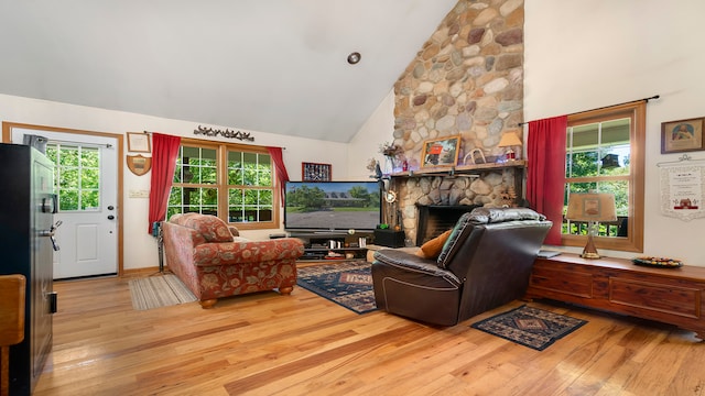 living room featuring light hardwood / wood-style floors, high vaulted ceiling, a wealth of natural light, and a stone fireplace