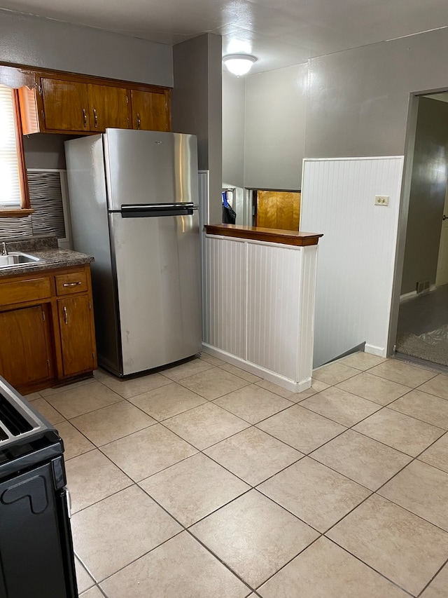 kitchen featuring electric range oven, sink, stainless steel refrigerator, light tile flooring, and tasteful backsplash