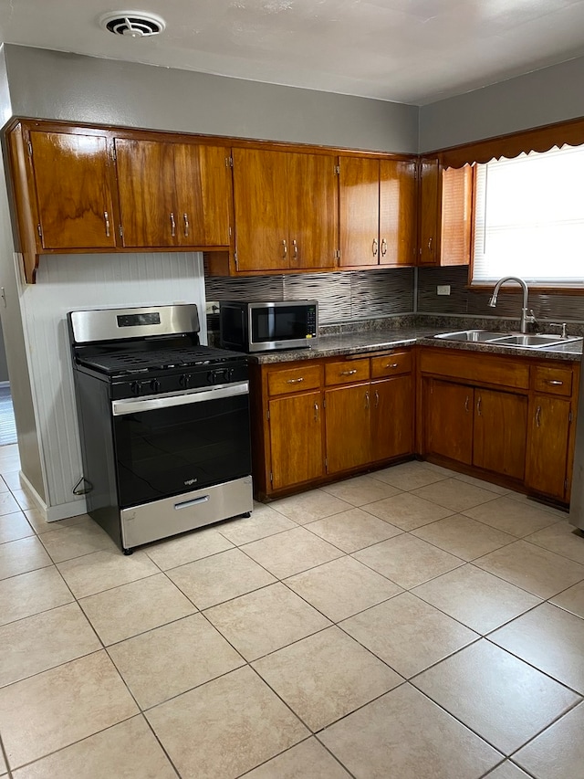 kitchen featuring light tile flooring, stainless steel appliances, sink, tasteful backsplash, and dark stone countertops