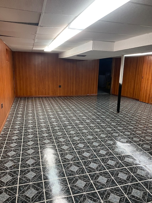 basement with a drop ceiling, wooden walls, and dark tile floors