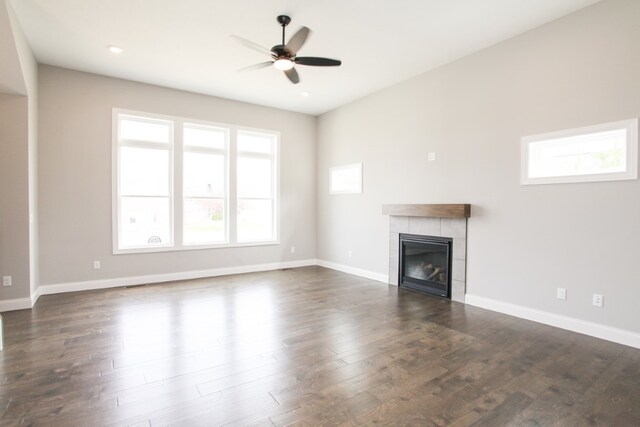 unfurnished living room with ceiling fan, a tile fireplace, and dark wood-type flooring