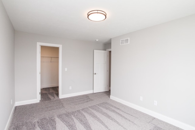 unfurnished bedroom with a spacious closet, a closet, and carpet flooring