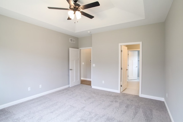 unfurnished bedroom with light carpet, ceiling fan, and a raised ceiling