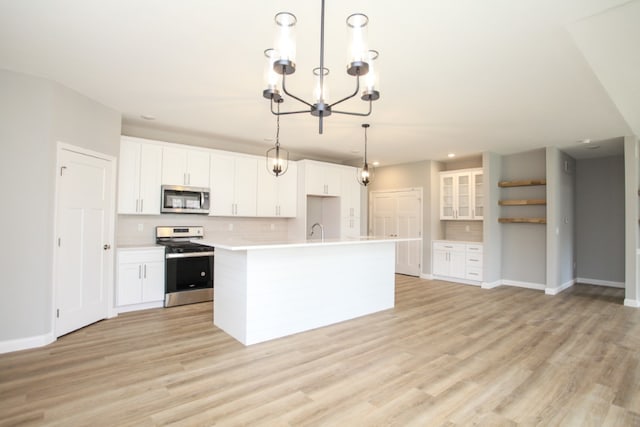 kitchen featuring appliances with stainless steel finishes, light wood-type flooring, white cabinetry, hanging light fixtures, and a center island with sink