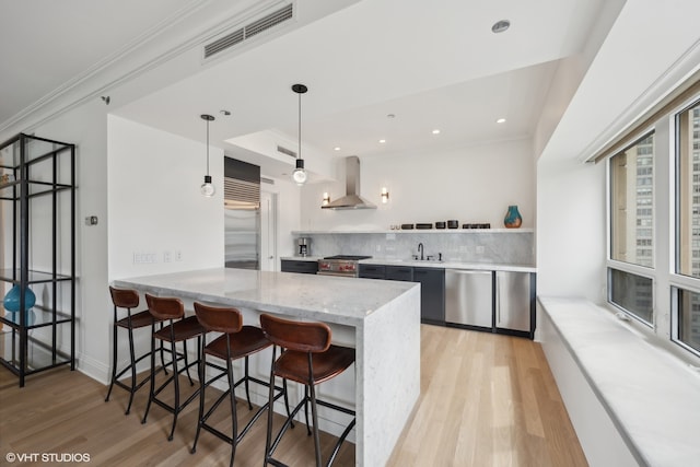 kitchen with decorative light fixtures, light hardwood / wood-style floors, high end appliances, tasteful backsplash, and wall chimney range hood