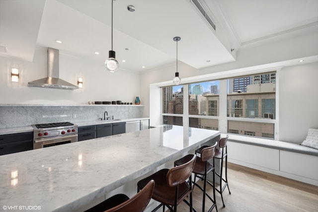 kitchen featuring light stone countertops, decorative light fixtures, backsplash, stainless steel appliances, and wall chimney exhaust hood