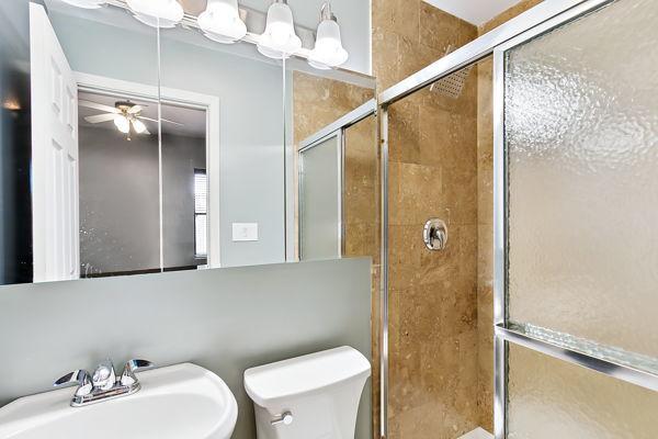 bathroom with toilet, sink, ceiling fan, and a shower with shower door