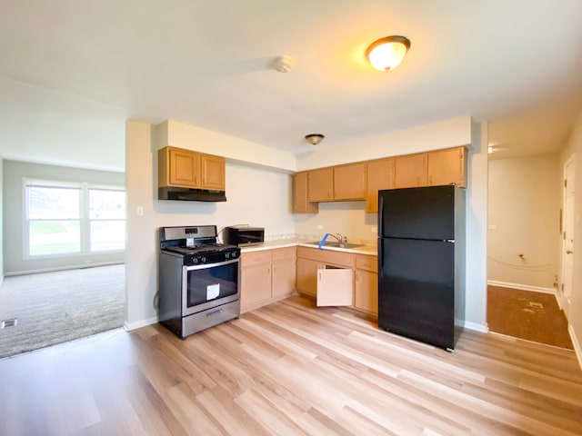 kitchen featuring light wood-type flooring, sink, black fridge, and stainless steel gas stove