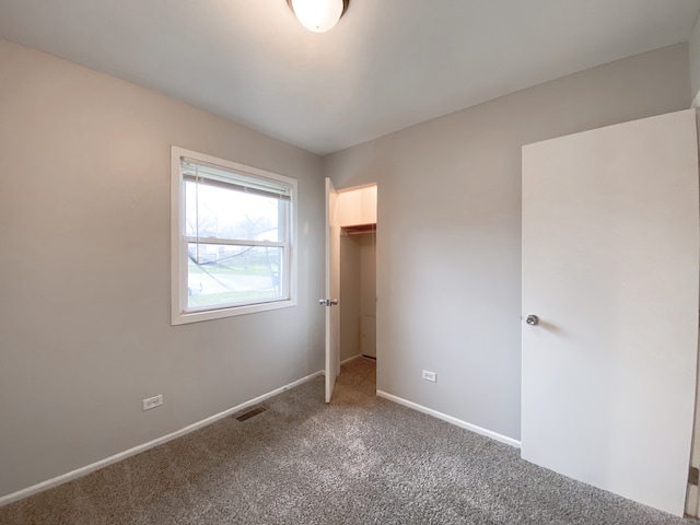 unfurnished bedroom featuring a closet, a walk in closet, and carpet flooring