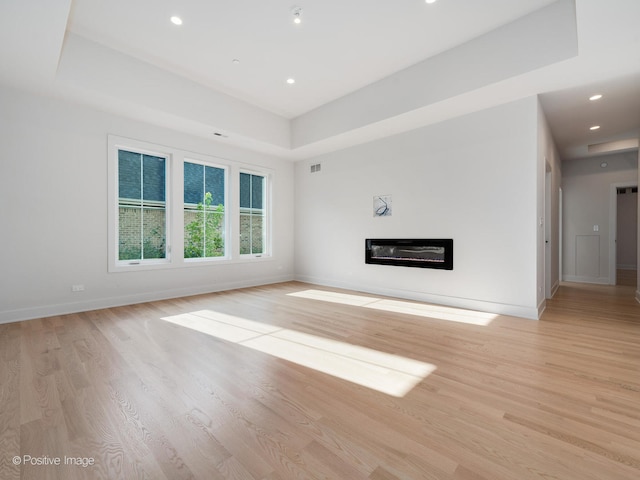 unfurnished living room featuring a tray ceiling and light hardwood / wood-style floors