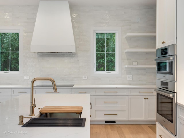 kitchen featuring stovetop, stainless steel double oven, white cabinetry, and light hardwood / wood-style flooring