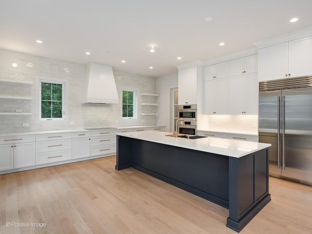 kitchen featuring white cabinets, premium range hood, stainless steel appliances, and light hardwood / wood-style flooring