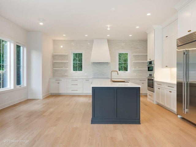 kitchen with light wood-type flooring, appliances with stainless steel finishes, premium range hood, and white cabinets