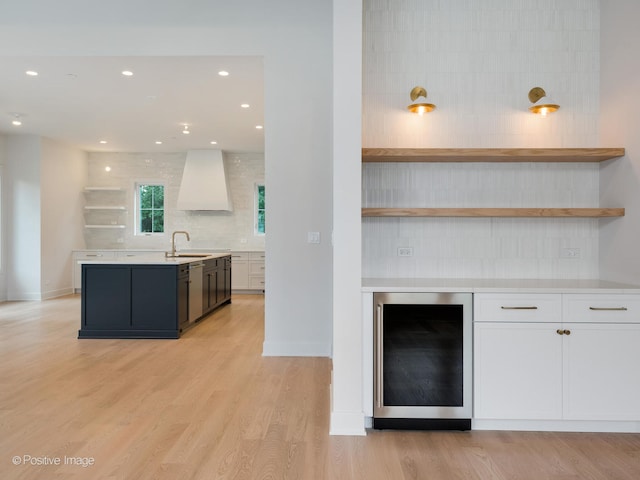 kitchen featuring light hardwood / wood-style flooring, beverage cooler, sink, premium range hood, and decorative backsplash