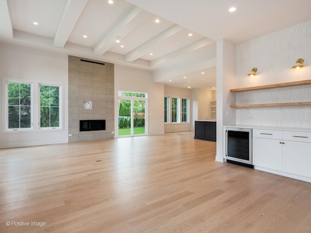 unfurnished living room with light wood-type flooring, tile walls, beverage cooler, and a tile fireplace