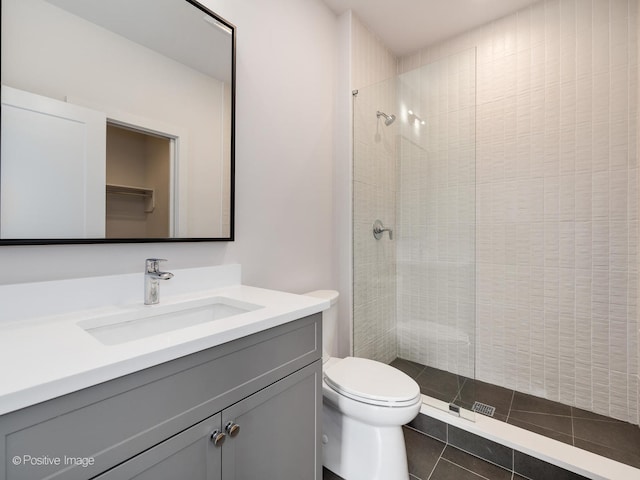 bathroom featuring vanity, toilet, a tile shower, and tile patterned floors