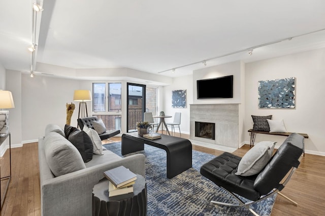 living area featuring track lighting, a fireplace, baseboards, and wood finished floors