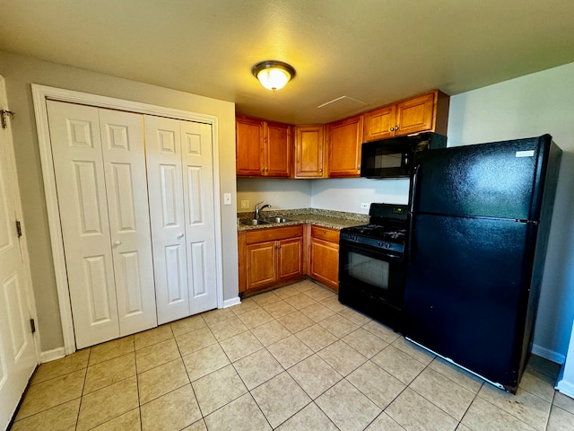 kitchen with stone countertops, black appliances, sink, and light tile flooring