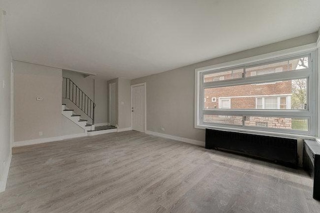 unfurnished living room with stairway, radiator heating unit, light wood-style floors, and baseboards