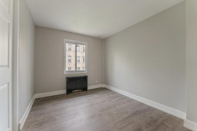 empty room with radiator heating unit, baseboards, and light wood-style flooring